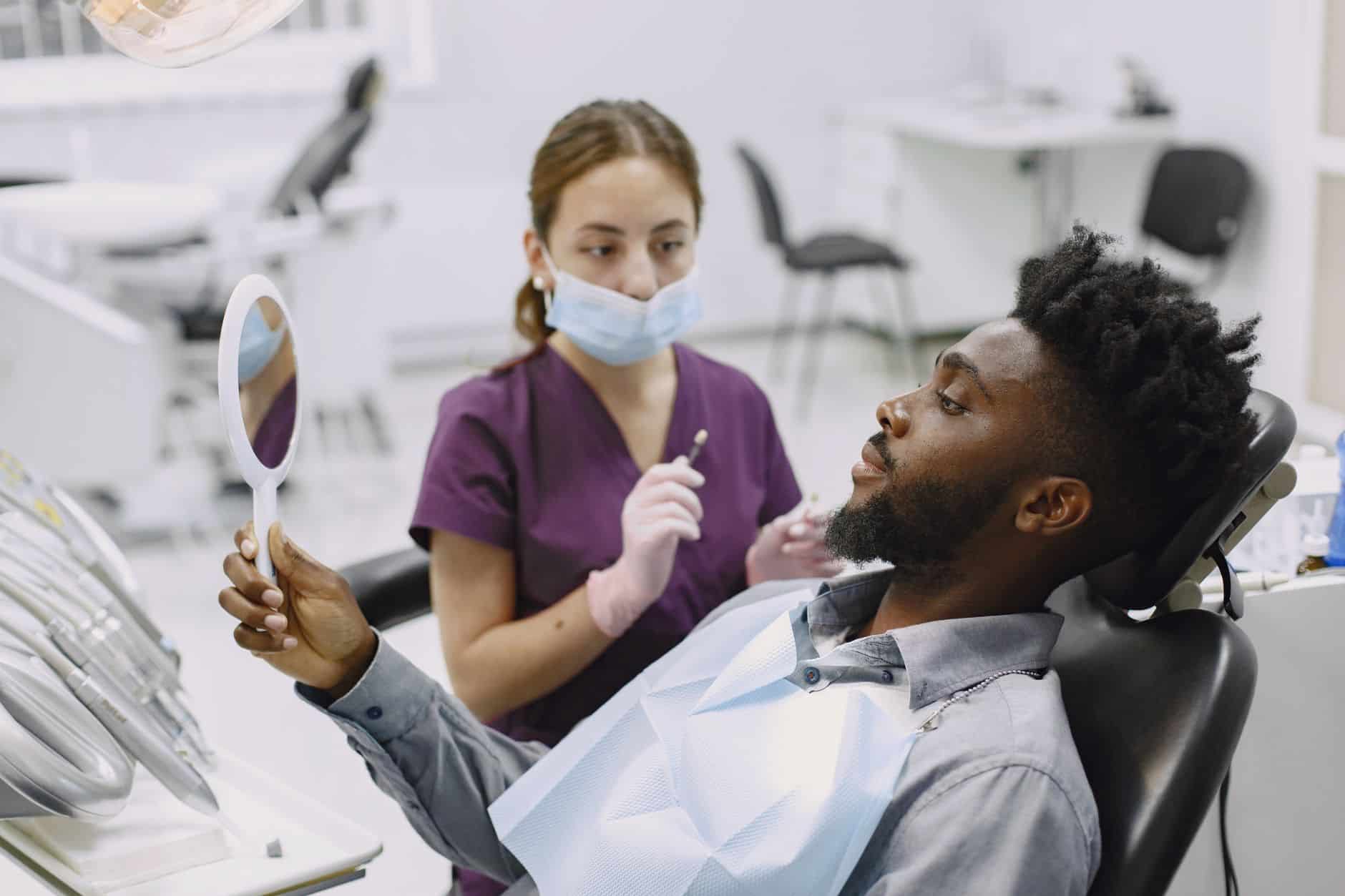 Paciente en el sillón dental revisando su boca con un espejo de mano junto a la odontóloga